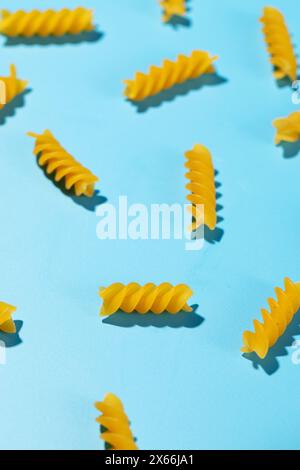 Spirales de pâtes fusilli non cuites dispersées sur un fond bleu dans un motif décoratif Banque D'Images