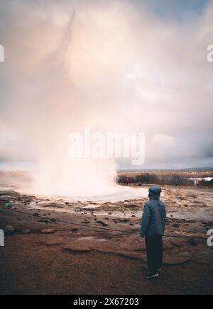 Geysir, Islande - octobre, 2023 : montre touristique femme faisant éruption geyser Strokkur. Strokkur fait partie de la zone géothermique. Banque D'Images