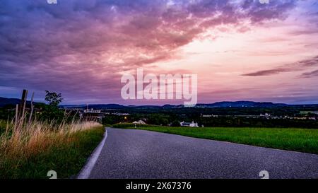 Rue étroite dans la soirée avec une belle rémanence. Vue sur le paysage suisse, avec plusieurs villages au loin. Banque D'Images