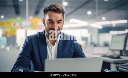 Occupé jeune homme d'affaires utilisant l'ordinateur portable dans le bureau moderne. Le manager réfléchit à des idées financières réussies. Homme heureux souriant de trouver des solutions de résolution de problèmes pour la compagnie. Banque D'Images