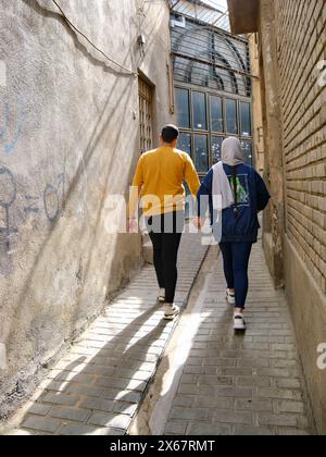 Un jeune homme et une jeune femme iraniens marchent ensemble en se tenant la main dans une ruelle étroite dans le centre historique de Shiraz, en Iran. Banque D'Images