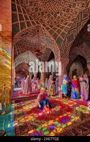 Une femme est assise dans la lumière des vitraux multicolores à l'intérieur de la mosquée Nasir al-Mulk du XIXe siècle, alias la mosquée rose. Shiraz, Iran. Banque D'Images