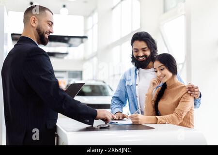 Un couple souriant signe des documents pour une voiture neuve à la salle d'exposition de l'établissement concessionnaire Banque D'Images