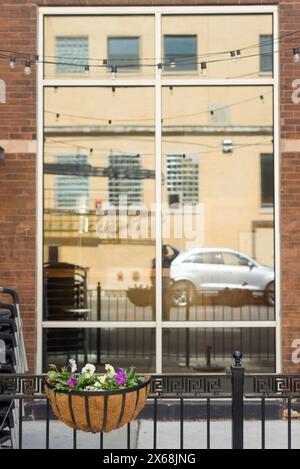 Une fenêtre avec une voiture dans le reflet. La voiture est blanche et garée devant un bâtiment Banque D'Images