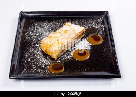 délicieux strudel décoré de sucre en poudre et de crème sur une plaque noire. Banque D'Images