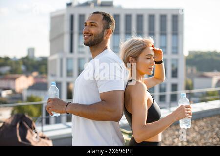 Athlétique fit femme se tient avec son dos à l'homme sportif musclé et boit de l'eau Banque D'Images