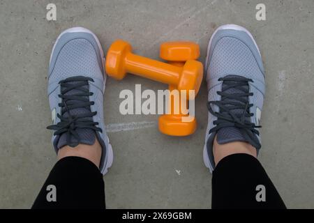 Concept fitness. Jambes féminines dans des chaussures de sport sur le sol avec des haltères. Banque D'Images