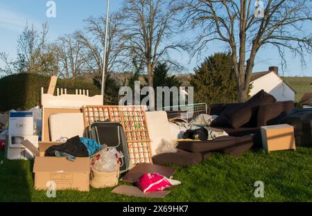Beaucoup de déchets dans une ville près de la haus. Grandes ordures avec vieux meubles en bois, jouets, boîtes, sacs en plastique dans une rue et l'herbe verte au printemps ensoleillé tra Banque D'Images