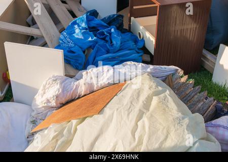 Beaucoup de déchets dans une ville près de la haus. Grandes ordures avec vieux meubles en bois, jouets, boîtes, sacs en plastique dans une rue et l'herbe verte au printemps ensoleillé tra Banque D'Images