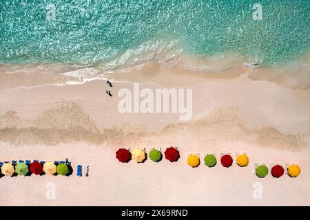 Vue aérienne de parasols colorés le long d'une plage avec deux marcheurs sur Rendezvous Bay à Anguilla. Banque D'Images