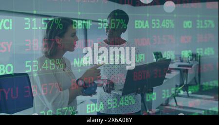 Image de la table de négociation sur diverses collègues féminines debout et discutant des rapports sur ordinateur portable Banque D'Images