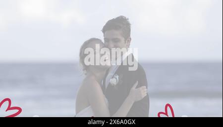 Couple caucasien embrassant sur la plage, à la fois en tenue formelle Banque D'Images