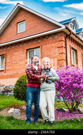 Couple marié russe mature serrant près du buisson fleuri de rhododendron, tenant un chien Banque D'Images