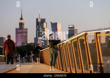 Varsovie, Pologne. 13 mai 2024. Une femme vue capturer le coucher de soleil sur la Vistule depuis le nouveau pont piétonnier et cycliste. Le nouveau pont piétonnier et cyclable sur la Vistule mesure 452 mètres de long et relie le centre-ville au quartier de Praga. Il a été ouvert le 28 mars 2024 et est devenu très populaire parmi les résidents de la ville et les touristes. Depuis le pont, les piétons et les cyclistes peuvent profiter de la vue sur la Vistule et Varsovie, y compris le centre historique - un site classé au patrimoine mondial de l'UNESCO. Crédit : SOPA images Limited/Alamy Live News Banque D'Images