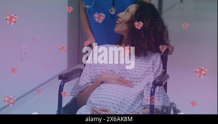 Image d'icônes de coeur sur une femme enceinte biraciale heureuse parlant avec l'infirmière Banque D'Images