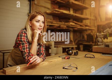 vue de côté sur la femme de menuisier après le travail, travail féminin comme charpentier en usine. tenez-vous à côté du bureau, réfléchissez Banque D'Images