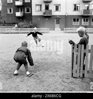 garçons des années 1950 jouant au football. Enfants jouant au football sur l'espace ouvert dans le salon. Le garçon est sur le point de frapper la balle et marquer dans le but imaginaire qui est gardé par un autre garçon. Roland Palm réf. 10-77-12 Banque D'Images