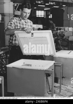 Congélateur dans les années 1950 Test final et installation de nouveaux congélateurs dans une usine. On voit un homme assembler et monter le couvercle d'un congélateur. Les aliments surgelés seraient le début d'une révolution dans les habitudes domestiques et le stockage des aliments. Beaucoup étaient sceptiques, et en particulier les fabricants d'aliments en conserve considéraient les aliments congelés comme une tendance passagère. Suède 1955 Banque D'Images