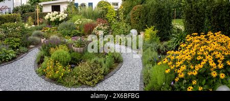 Vue panoramique sur le jardin avec un petit chemin à travers une variété de fleurs, d'herbes et d'arbustes Banque D'Images