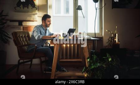 Jeune homme beau travaille sur un ordinateur portable dans Agence créative dans Loft Office. Décoration élégante rénovée avec plantes maison, affiches artistiques et grandes fenêtres. Banque D'Images