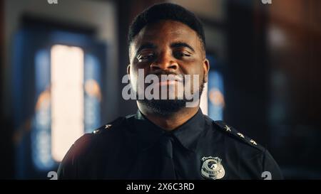 Portrait authentique de policier noir heureux et beau en uniforme universel souriant à la caméra. Agent afro-américain chargé de l'application de la loi. Gardien de sécurité de la salle d'audience au travail. Banque D'Images