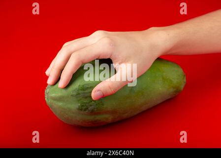 Main masculine sur une papaye verte. Isolé sur fond rouge. Banque D'Images