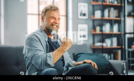 Charismatique homme barbu assis sur un canapé regarde le jeu à la télévision, célèbre le sport quand l'équipe gagne le championnat. Concentré, joyeusement intense et auteure de fan quand le club préféré joue Banque D'Images