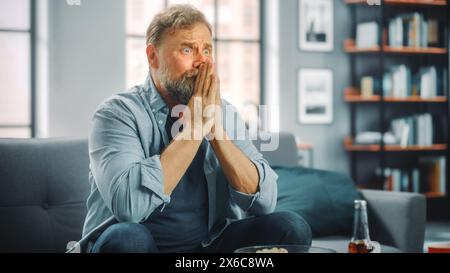 Charismatique homme barbu assis sur un canapé montres jeu à la télévision, inquiétant pour son équipe de football. Concentré, joyeusement intense et auteure de fan quand le club préféré joue Banque D'Images