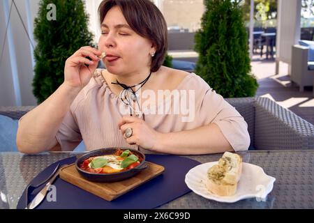 Une femme de taille moyenne en robe fuzz pêche mangeant Shakshouka dans un restaurant moderne Banque D'Images