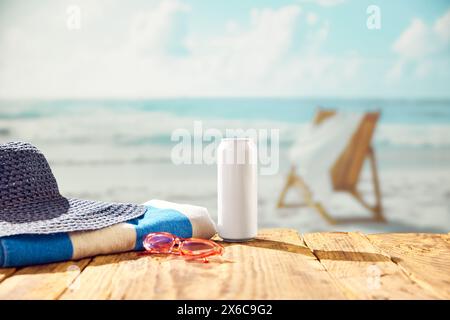 Rafraîchissement en bord de mer. Bouteille de bière avec chapeau et serviette sur la plage avec belle vue sur l'océan. Banque D'Images