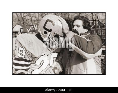 Un entraîneur de l'équipe de football de l'école secondaire Canarsie félicite un joueur après une victoire en lui serrant la main et en tapotant son casque. Au Midwood Field à Brooklyn en 1982. Banque D'Images