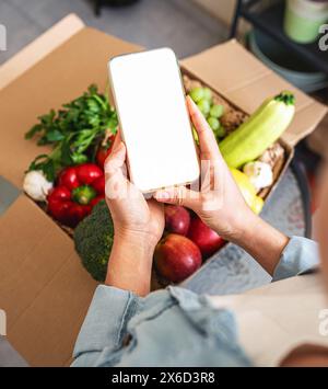 Maquette de l'écran blanc du téléphone intelligent au-dessus de la ferme des légumes cultivés dans le carton Banque D'Images