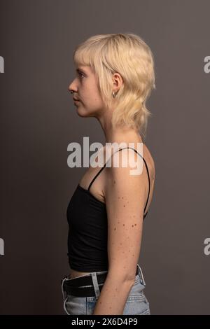 Portrait de profil d'une femme blonde dans un top noir et un Jean, photographie de studio mettant en valeur la mode et le style personnel, fond neutre. Banque D'Images