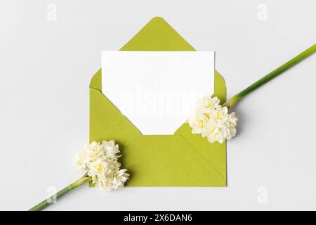 Enveloppe verte avec feuille de papier blanche propre pour votre texte et fleurs de printemps jonquilles blanches sur fond gris. Invitation aux fêtes. Plat l Banque D'Images