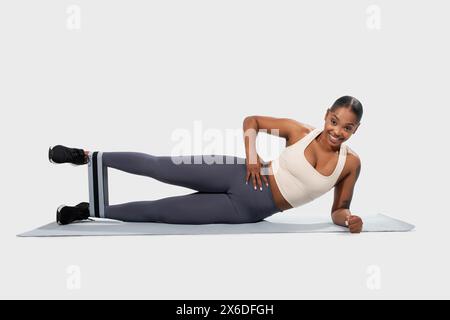 Femme souriante effectuant un exercice de planche latérale avec bande de résistance Banque D'Images