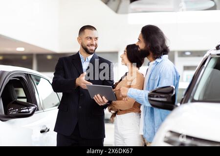 Vendeur de voitures souriant présentant les options aux acheteurs potentiels au Showroom Banque D'Images