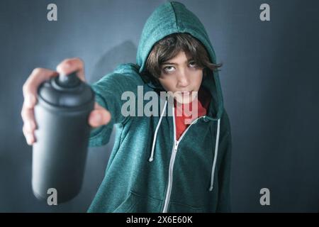 Un jeune homme dans un sweat à capuche vert pulvérise des graffitis sur un mur. La bombe aérosol est noire et le mur est gris. La scène est rebelle et avant-gardiste Banque D'Images
