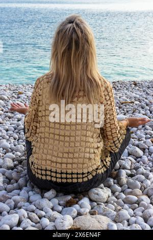 L'image capture un portrait serein d'une belle femme en méditation sur une plage de galets. Banque D'Images