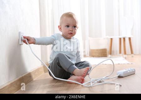 Petit enfant jouant avec la prise électrique et la prise de la barrette d'alimentation à la maison. Situation dangereuse Banque D'Images