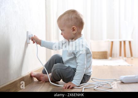 Petit enfant jouant avec la prise électrique et la prise de la barrette d'alimentation à la maison. Situation dangereuse Banque D'Images