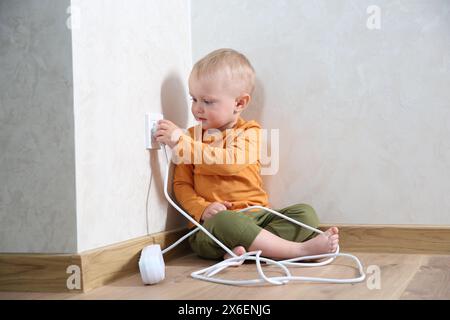 Petit enfant jouant avec la prise électrique et la prise de la barrette d'alimentation à la maison. Situation dangereuse Banque D'Images