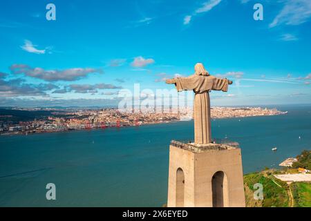 Vue aérienne de la statue du Christ Roi surplombant le Tage et le paysage urbain sous le ciel bleu. Vue plongeante sur le monument catholique et la ville. Lisbonne, Portugal Banque D'Images