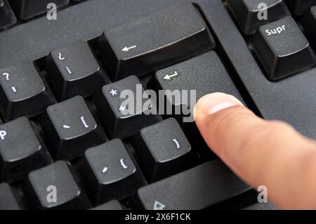 Gros plan de l'index appuie sur la touche entrée du clavier noir Banque D'Images