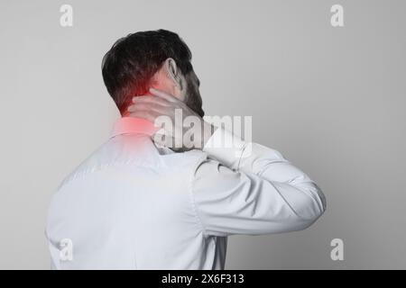 Homme souffrant de douleurs au cou sur fond gris, effet noir et blanc Banque D'Images
