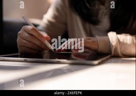 Image recadrée d'une femme tenant un stylet, écrivant sur une tablette numérique, assise à une table près de la fenêtre par une journée ensoleillée. écrire, esquisser, tak Banque D'Images