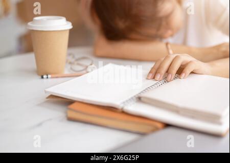 Une jeune étudiante asiatique fatiguée et endormie s'endort sur la table en faisant ses devoirs ou en lisant un livre. concept d'éducation Banque D'Images