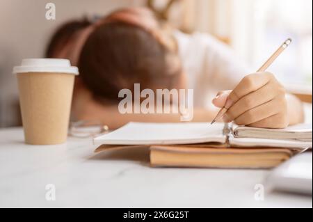 Une jeune étudiante asiatique fatiguée et endormie tient un crayon, s'endort sur la table en faisant ses devoirs ou en lisant un livre. étudiant paresseux, Banque D'Images