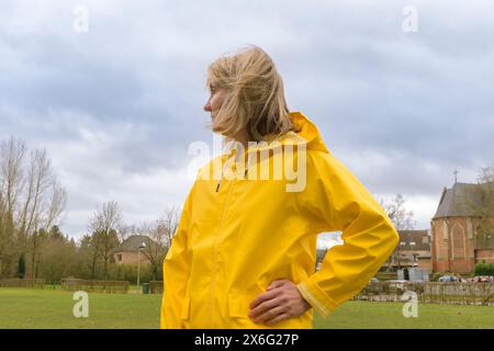 Portrait d'une jeune femme vêtue d'un imperméable jaune posant avec un ciel sombre nuageux à capuche. Caucasien Banque D'Images