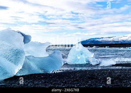 Un gros morceau de glace repose dans le sable. Le ciel est nuageux et l'eau est bleue Banque D'Images