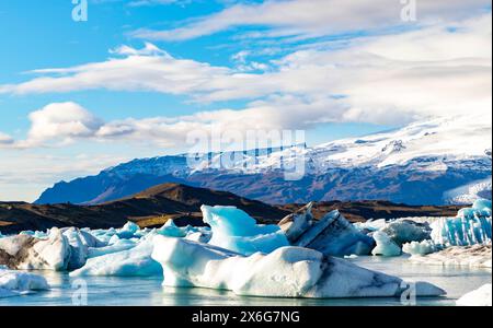 Une grande masse d'eau est couverte de glace, avec des montagnes en arrière-plan. Le ciel est clair et bleu, et la scène est paisible et sereine Banque D'Images